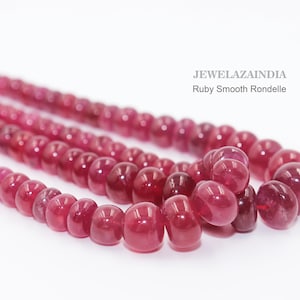 Puede incluir: Un hilo de cuentas rondelle de rubí lisas de color rojo rosado intenso, dispuestas en una línea curva. El texto JEWELAZAINDIA Ruby Smooth Rondelle está impreso en la esquina superior derecha. Las cuentas tienen un acabado pulido, brillante y uniforme.
