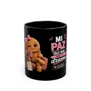 May include: A black ceramic mug featuring a cartoon gingerbread character with a pink bow sitting in a pink armchair, holding a small cup. The text reads: MI PAZ VALE MÁS QUE TU DRAMA, NO ES EGOÍSMO ES AMOR PROPIO, and MODO PAZ Y ENFOCADA.