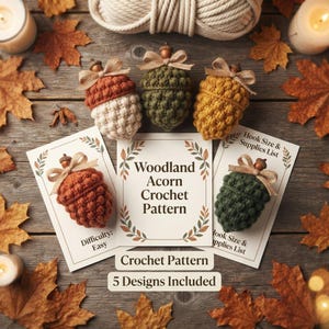 Op de afbeelding: Vijf gehaakte eikels in roest, crème, olijfgroen en mosterdgeel, elk bekroond met een kleine houten kraal en een jute strik. Twee gedrukte kaarten tonen de tekst Woodland Acorn Crochet Pattern, Difficulty: Easy en Hook Size & Supplies List.