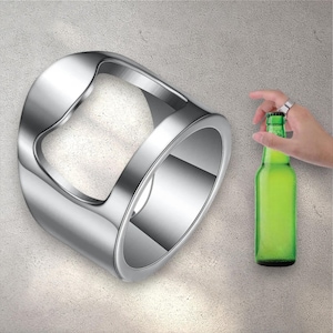 May include: A shiny, silver bottle opener ring with a curved design. The ring is next to a green glass bottle. The ring is being used to open the bottle.