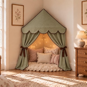 May include: A sage green corner play tent featuring a scalloped canopy edge with dark brown trim, matching tie-backs, and a soft tufted floor cushion. Inside, the tent is illuminated by string lights and filled with various patterned throw pillows.