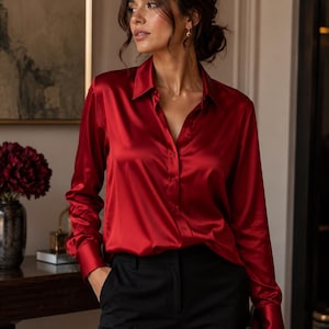 May include: A vibrant red satin button-down shirt with long sleeves and a classic collar. The shirt is paired with black trousers. The fabric has a lustrous sheen, reflecting light. The overall style is elegant and sophisticated.