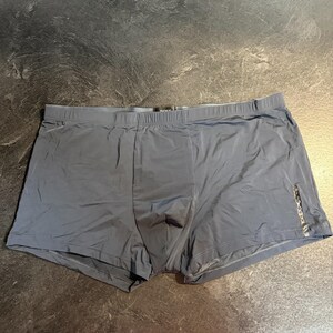 May include: A pair of dark gray boxer briefs featuring an elastic waistband with the text BOSS centered at the top. The garment includes a vertical decorative strip with small circular metallic accents positioned on the lower right side panel.