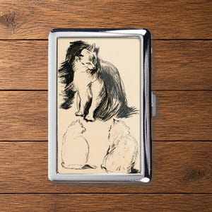 May include: A rectangular metal case featuring a cream-coloured insert with black ink illustrations of three cats. One cat is depicted in a detailed seated pose, while two other cats are shown from behind in simpler outlines on a light background.