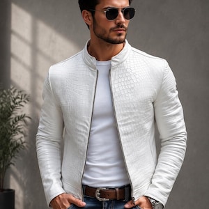 May include: A white jacket with a textured crocodile skin pattern, featuring a stand-up collar and a full-length silver zipper. The jacket is worn over a plain white t-shirt, paired with blue denim jeans and a brown leather belt with a silver buckle.