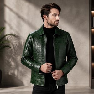Peut inclure: Une veste vert foncé avec un motif texturé en peau de crocodile, un col classique et une fermeture éclair frontale intégrale. Le vêtement est porté sur un pull à col roulé noir, présentant une coupe structurée avec des manches longues.