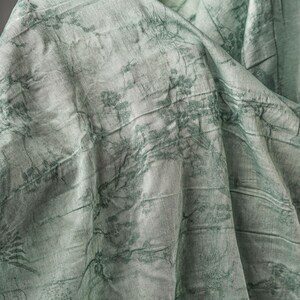 May include: A light mint green fabric featuring a dark green printed pattern of delicate branches and foliage. The material has a visible crinkled texture with folds and drapes that create depth and shadows across the surface of the textile.