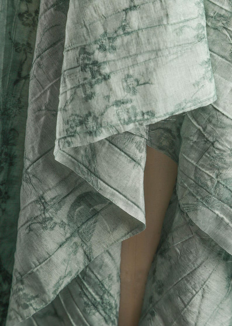 May include: A light green fabric with a darker green botanical print featuring birds and branches. The material has a visible quilted texture with diagonal stitching lines running across the surface, creating a layered and draped appearance.