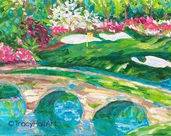 May include: An impressionistic painting of a golf course scene. The artwork features a bridge over a body of water, with vibrant green grass, pink and white flowers, and a yellow flag. The artist's signature is visible in the bottom left corner.