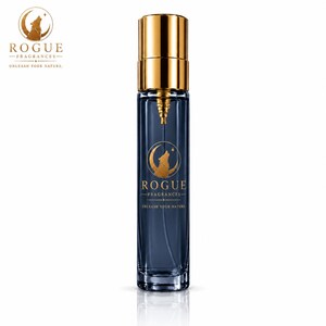 May include: A tall, cylindrical glass perfume bottle with a dark blue tint and a metallic gold cap. The front features a gold logo of a wolf howling at a crescent moon, with the text ROGUE FRAGRANCES UNLEASH YOUR NATURE printed below.