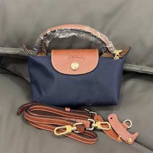 May include: A navy blue handbag with a brown leather flap and handle. The bag has a gold-colored clasp and a detachable brown leather strap. The bag is made of a durable material and is designed for everyday use.