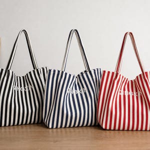 May include: Three tote bags with vertical stripes in black, navy blue, and red, each featuring white stripes and the text QINGXIN embroidered in white on the front. The bags have two shoulder straps and a structured, open-top design.