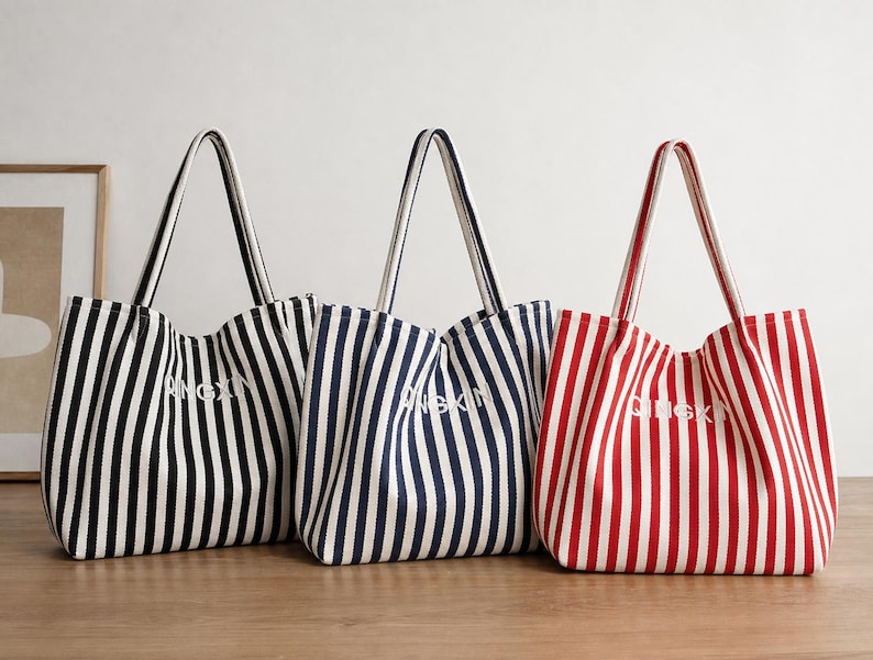 May include: Three tote bags with vertical stripes in black, navy blue, and red, each featuring white stripes and the text QINGXIN embroidered in white on the front. The bags have two shoulder straps and a structured, open-top design.