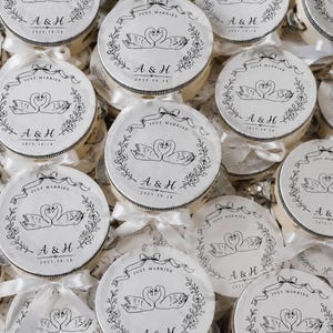 Könnte beinhalten: Eine Sammlung runder weißer Tamburine mit einer schwarzen Tuschezeichnung von zwei Schwänen, die ein Herz bilden, umgeben von einem Blumenkranz und einem Banner mit dem Text "JUST MARRIED", "A & H" und dem Datum "2025.10.18".