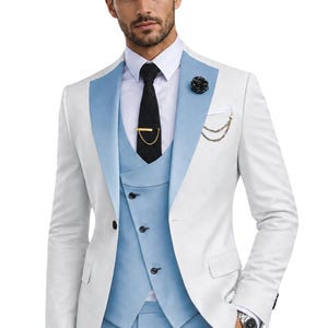 May include: A white blazer with light blue lapels, a light blue waistcoat with three buttons, light blue trousers, a white dress shirt, a black necktie with a gold tie bar, a black lapel flower, and a gold chain accessory on the chest pocket.