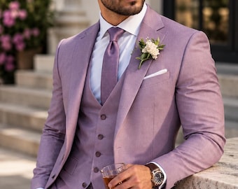 May include: A lavender three-piece suit consisting of a blazer, a button-down vest, and trousers. The suit is paired with a white dress shirt, a matching lavender tie, a white pocket square, and a small white floral boutonniere on the lapel.