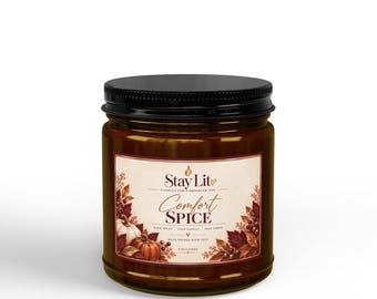 May include: A brown candle in a glass jar with a black lid. The label features the text Stay Lit, Comfort Spice, Warm Spices, Cozy Vanilla, Soft Amber, and 9 oz candle, decorated with illustrations of pumpkins, berries, and autumn leaves.