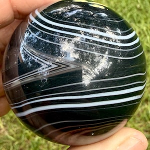 Puede incluir: Una piedra pulida de forma esférica que presenta bandas alternas de negro profundo y blanco nítido. La superficie es lisa y reflectante, mostrando un patrón natural de capas que envuelve toda la forma globular del espécimen mineral.