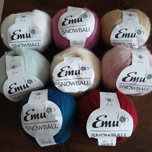 May include: Eight balls of Emu Snowball yarn in various colours including white, pink, tan, light green, cream, dusty rose, dark blue, and deep red. Each ball features a white paper label with the Emu Snowball logo and a graphic of yarn.