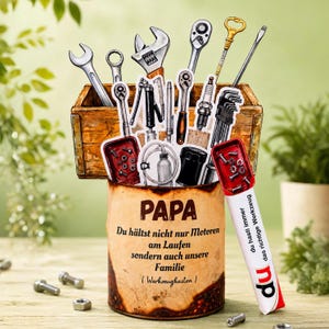 May include: A Father's Day gift featuring a wooden toolbox and a rusty can filled with various tools. The can has the word "PAPA" and a message in German. A red and white marker with the text "du hasti immer das richtige Werkzeug" is also included.