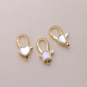 May include: Three gold-toned lobster claw clasps featuring decorative shapes with iridescent white shell inlays. One clasp has a heart shape, one has a star shape, and one has a teardrop shape, each with a functional spring-loaded mechanism.