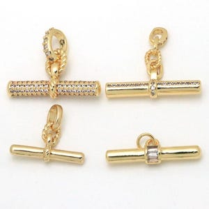May include: Four gold-toned toggle clasps for jewellery making. Two clasps feature horizontal bars embedded with small clear crystals, one has a plain bar with a central crystal baguette, and one is a plain gold bar with a twisted loop connector.