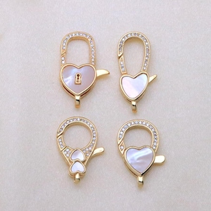 May include: Four gold-toned metal jewelry clasps featuring heart-shaped mother-of-pearl inlays and clear crystal accents. The clasps include two elongated heart shapes, one circular shape with two small hearts, and one circular shape with a single heart.