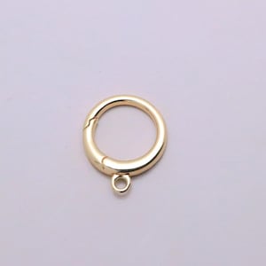 May include: A gold-toned circular spring ring clasp featuring a smooth, polished finish and a small, integrated loop at the bottom for attachment. The clasp mechanism is visible along the side of the ring, allowing it to open and close securely.