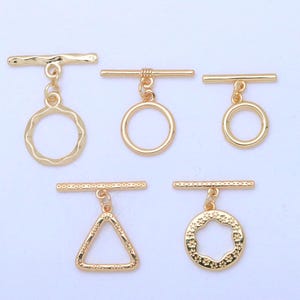 May include: Five gold-colored toggle clasps in various designs. The clasps include a textured circle, a smooth circle, a small circle, a triangle, and a textured hexagon. Each clasp has a horizontal bar attached.