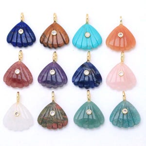 May include: A collection of twelve fan-shaped pendants carved from various colorful gemstones. Each pendant features a gold-toned metal bail at the top and a small, round, clear stone set in the center of the ribbed, shell-like surface.