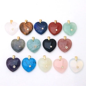 May include: A collection of thirteen heart-shaped gemstone pendants in various colors including white, brown, blue, red, green, grey, black, pink, and turquoise. Each pendant features a gold-toned metal bail and a single small embedded clear stone.