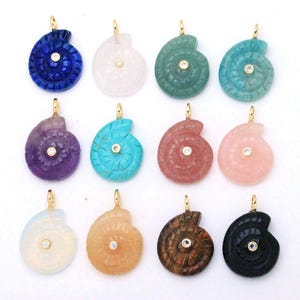 May include: Twelve spiral-shaped pendants carved from various gemstones, including blue, pink, green, purple, and black varieties. Each pendant features a central round clear stone set in a gold-toned metal bail at the top for hanging.