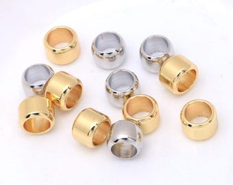 May include: A collection of small, cylindrical metal beads in polished gold and silver tones. Each bead features a smooth, rounded exterior surface and a hollow center, designed for threading. The assortment includes several individual pieces.