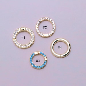 Könnte beinhalten: Vier goldfarbene kreisförmige Ringe, beschriftet mit #1, #2, #3 und #4. Ring #1 verfügt über ein Scharnier und klare Steine. Ring #2 ist ein kreisförmiges Band mit klaren Steinen. Ring #3 ist ein kleineres Band mit türkis farbenen Steinen.