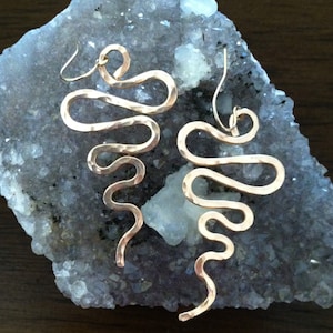 May include: A pair of gold-toned earrings with a hammered, wavy design. The earrings are long and dangle, with a hook closure.