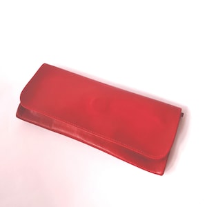 Peut inclure: Un portefeuille pochette rectangulaire en cuir rouge avec une finition lisse et une fermeture à rabat. Le portefeuille présente un profil fin et allongé avec des bords nets et une couleur rouge vive uniforme sur toute la surface extérieure.