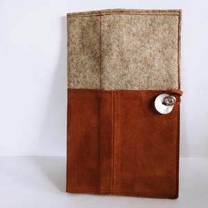 May include: A rectangular case featuring a top section of textured beige felt and a bottom section of smooth rust-colored suede. The case is secured with a thin leather cord wrapped around a circular white mother-of-pearl button closure.