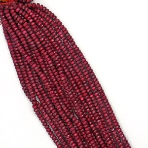 Può includere: Una lunga fila di piccole perline di rubino sfaccettate di colore rosso intenso, disposte in diverse file parallele. Le perline sono rotonde e presentano una finitura opaca e testurizzata, infilate su un sottile cordino rosso visibile in alto.
