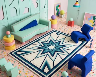 Op de afbeelding: Een rechthoekig vloerkleed met een centraal sterpatroon in blauw- en wittinten, omringd door een mintgroene bank, twee blauwe gebogen stoelen en diverse geometrische accentstukken in een kamer met een roze en veelkleurige terrazzovloer.