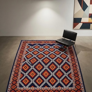 Könnte beinhalten: Ein rechteckiger Teppich mit dunkelblauem Hintergrund und einem sich wiederholenden geometrischen Muster aus orangefarbenen, roten und gelben Rauten, die weiß umrandet sind. Der Teppich hat eine breite Bordüre mit kleinerem Rautenmotiv.
