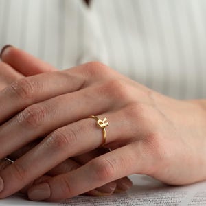 Minimalist ring worn on hand featuring a script initial ring with elegant handwriting lettering