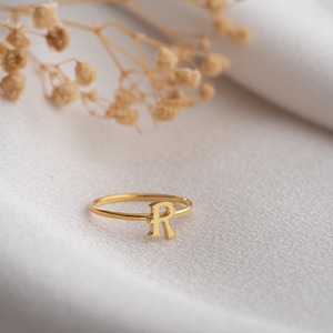 Custom ring displayed on a neutral background featuring a script initial ring with handwriting lettering