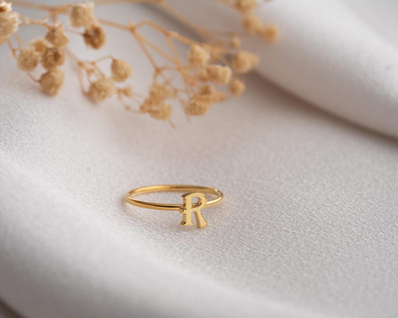 Custom ring displayed on a neutral background featuring a script initial ring with handwriting lettering