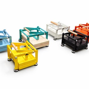 May include: A collection of colorful, small wooden presses. Each press features a rectangular base, a hinged top, and a wooden handle. The presses are painted in various colors, including blue, green, yellow, white, black, and orange.