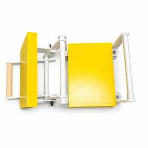 May include: A yellow and white wooden table saw with a light brown handle. The saw has a rectangular yellow blade guard and a yellow table surface. The frame is white.