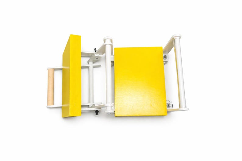 May include: A yellow and white wooden table saw with a light brown handle. The saw has a rectangular yellow blade guard and a yellow table surface. The frame is white.
