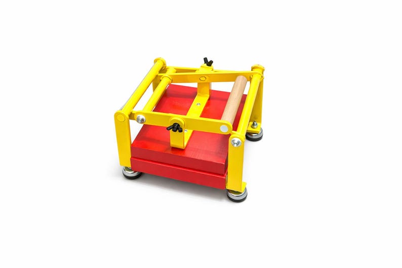 May include: A bright yellow and red printing press with a wooden roller. The press has a rectangular red base and a yellow frame. The press is designed for printmaking and crafting.