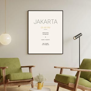 May include: A framed wall art print featuring the text JAKARTA, 05.48 PM, almost home not quite yet, 6.2088 S / 106.8456 E, and DAY / PHASE CITY PHASE 04 in black and gold lettering on a cream background, displayed in a thin black frame.