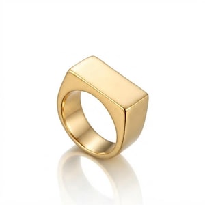 Peut inclure: Une bague chevalière dorée polie présentant une surface supérieure plate et rectangulaire lisse ainsi qu'un anneau solide et épais. La bague possède une finition métallique réfléchissante et un design géométrique épuré qui s'affine légèrement.