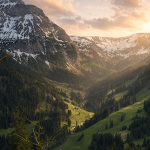 Könnte beinhalten: Eine Gebirgstal-Landschaft mit schneebedeckten Gipfeln, dichten Nadelwäldern und leuchtend grünen Wiesen. Die Szene wird vom warmen, goldenen Licht des Sonnenuntergangs beleuchtet, während sanfte Wolken über dem schroffen Gebirgszug ziehen.